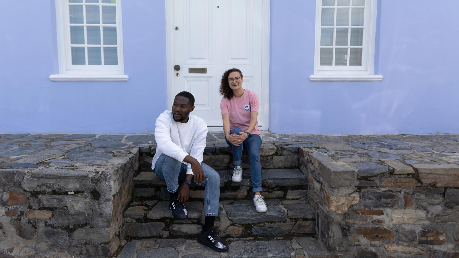 a man and woman sitting on stone steps in front of a blue building